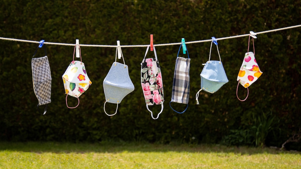 Des masques de différentes couleurs et de différents formats accrochés sur une corde à linge.