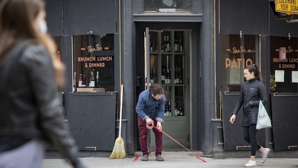 Un homme marque le trottoir devant son commerce pour faciliter la distanciation physique.