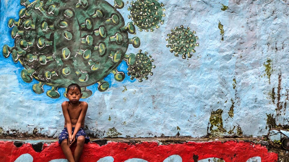 Un jeune garçon assis devant une murale représentant le coronavirus.