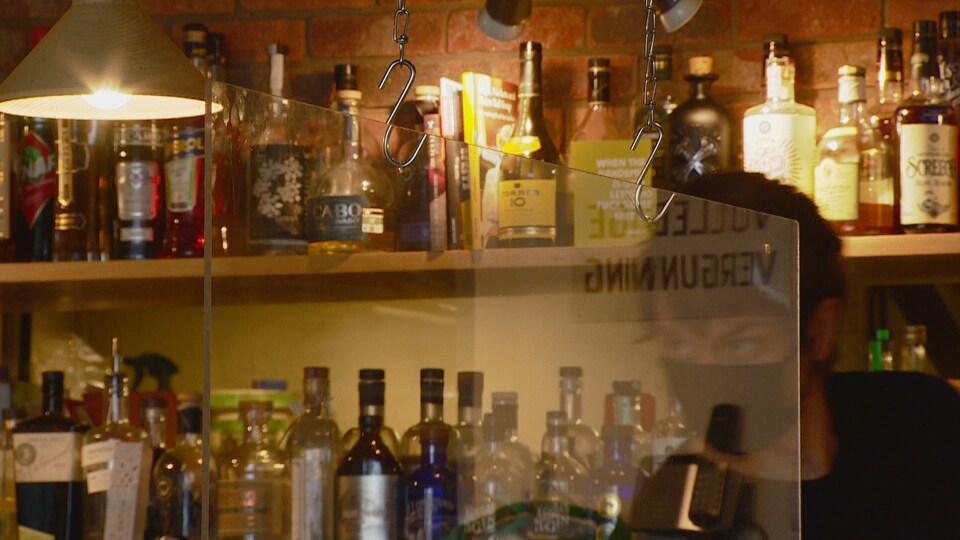 Un barman derrière une séparation en plexiglas dans un bar.