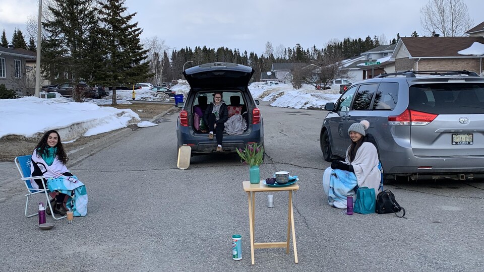 Trois jeune femmes assises sur des chaises dans la rue.