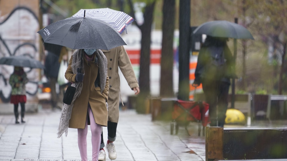 Une personne qui marche dehors et dont le visage est caché par un parapluie porte un masque jetable.