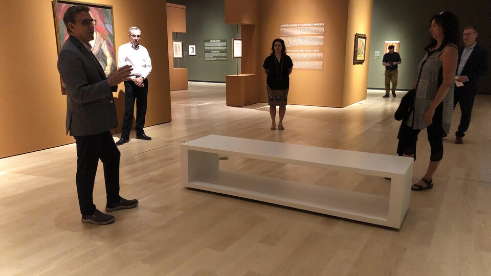 Des visiteurs dans une salle du musée écoutent un homme parler.