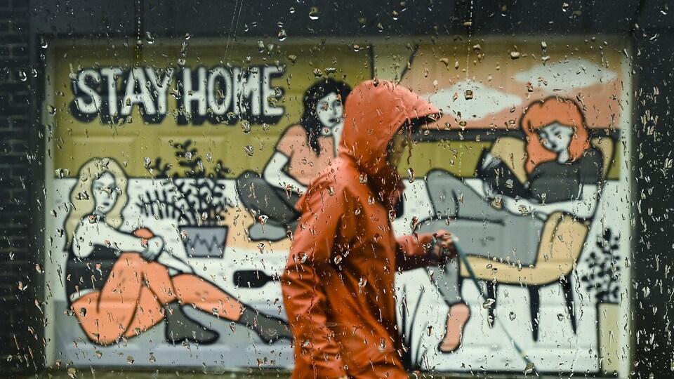 Un passant, sous la pluie, marche devant une murale intitulée Stay Home.