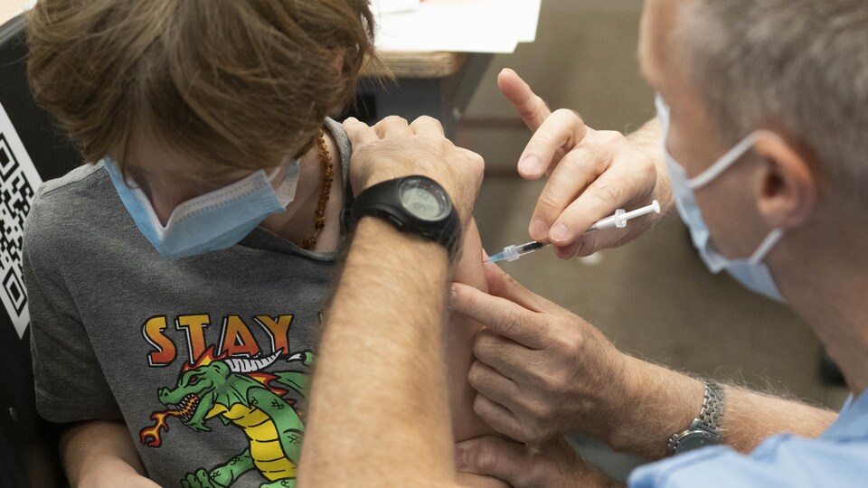 Un enfant baisse la tête alors qu'il reçoit une injection.