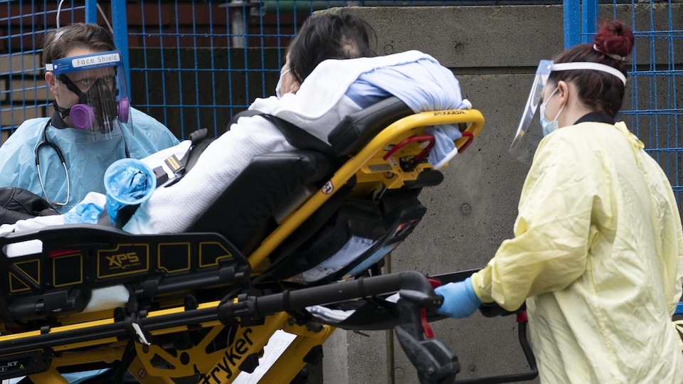 Une patiente est transportée par deux travailleurs de la santé, sur une civière. 