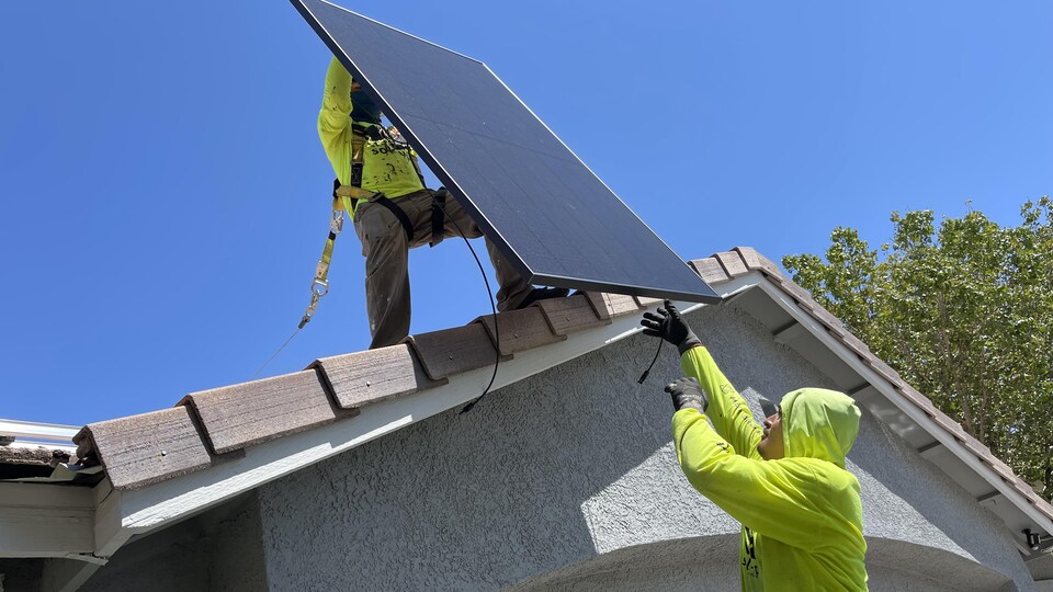 Deux ouvriers installent des panneaux solaires sur le toit d'une maisons.