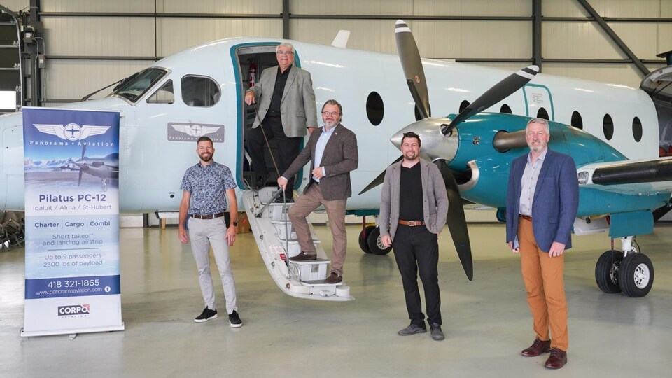 Cinq hommes se tiennent debout tout près d'un petit avion.