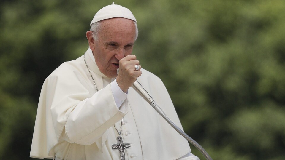 Le pape François est debout devant un micro en train de prononcer un discours en levant le poing.