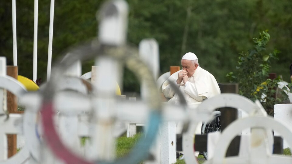 Le pape François, assis sur un fauteuil roulant, se recueille dans un cimetière face à des tombes.