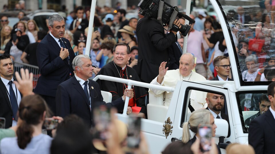 Le pape et l'archevêque souriants saluent la foule massée le long de la rue lors de son passage en papemobile