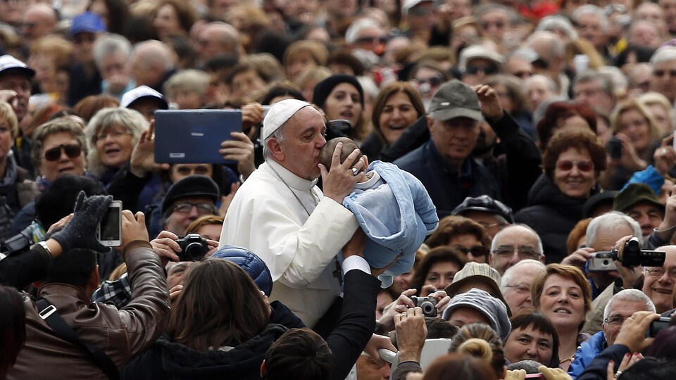 Le pape François et un bébé, au milieu de centaines de personnes.