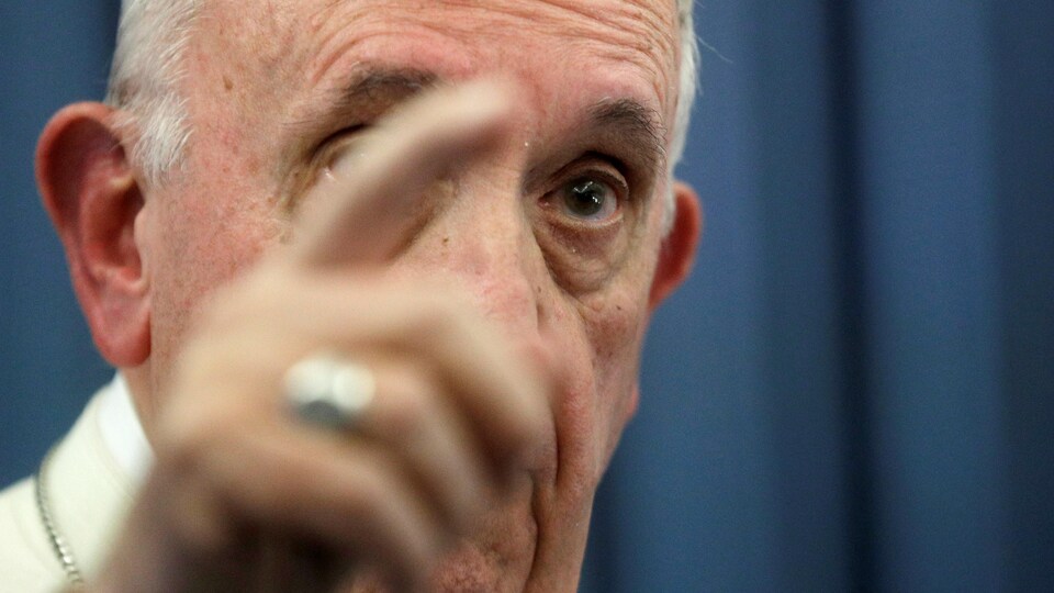 Le pape François pointe du doigt en s'exprimant devant des journalistes.