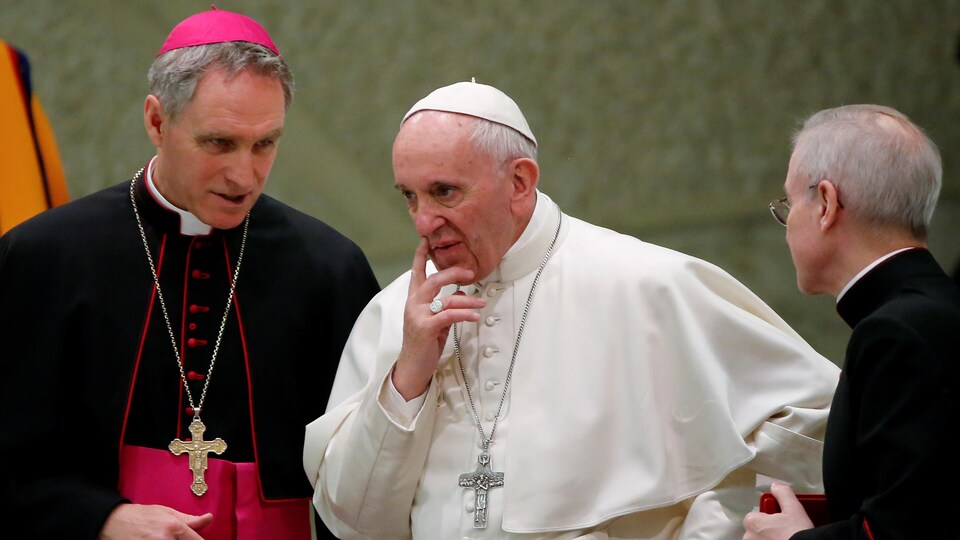 Le pape François, au Vatican, regarde devant soi en touchant le coin de la bouche avec son index.