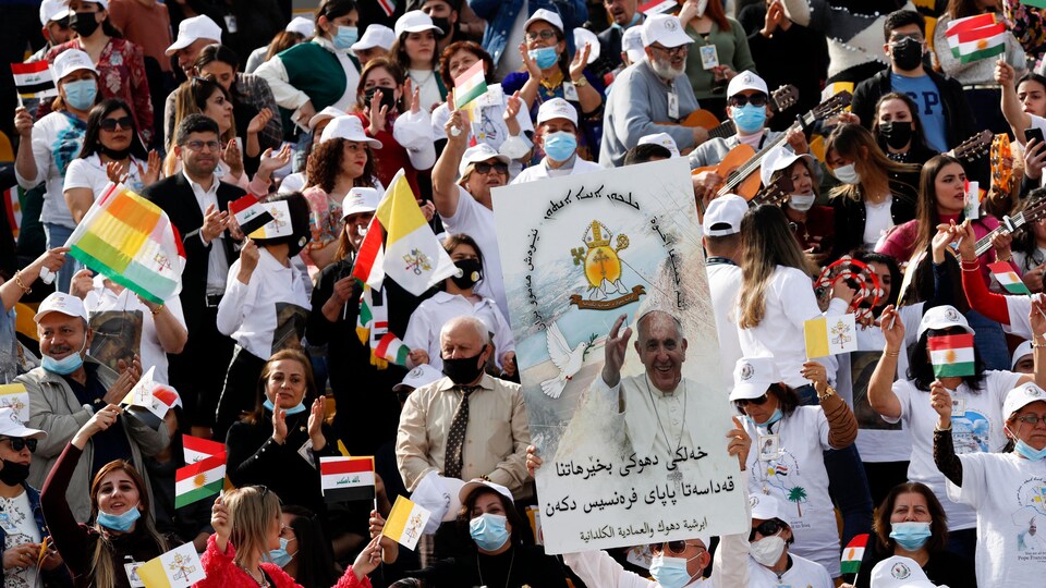 Des Irakiens agitent des drapeaux kurdes et nationaux en attendant l'arrivée du pape François au stade Franso Hariri d'Arbil, le 7 mars 2021, dans la capitale de la région autonome kurde du nord de l'Irak.