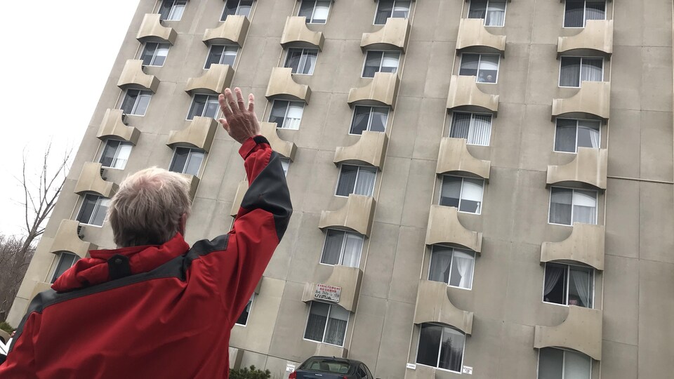 Un homme envoie la main à sa mère à la fenêtre du cinquième étage.