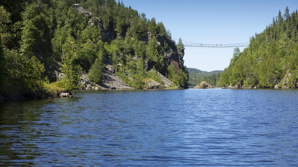 Vue sur un lac situé entre deux montagnes, reliées par un pont suspendu.