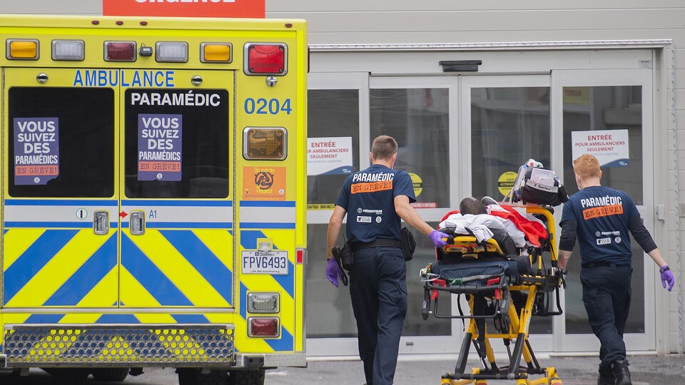 Une ambulance; des ambulanciers poussent un brancard. 