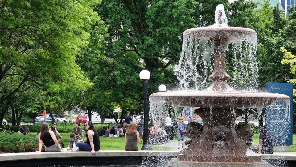 Des gens assis autour d'une fontaine dans un parc. 