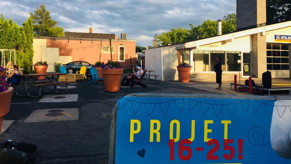 Une affiche sur laquelle est écrit « Projet 16-25 » devant des tables à pique-nique et des chaises de jardin.