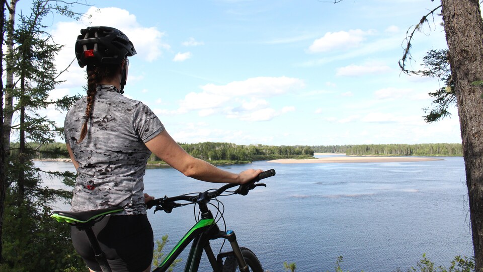 Une femme à côté de son vélo regarde une rivière.