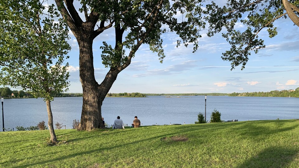 Trois personnes assises sur l'herbe regardent le lac Osisko à Rouyn-Noranda.