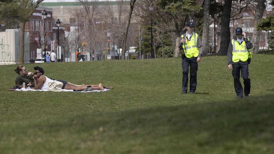 Deux agents de la ville marchent près de deux personnes allongées dans un parc.