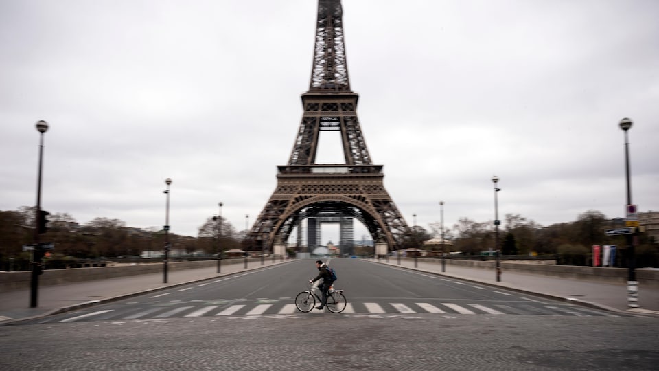 Un homme à vélo traversent une rue déserte sous la Tour Eiffel.