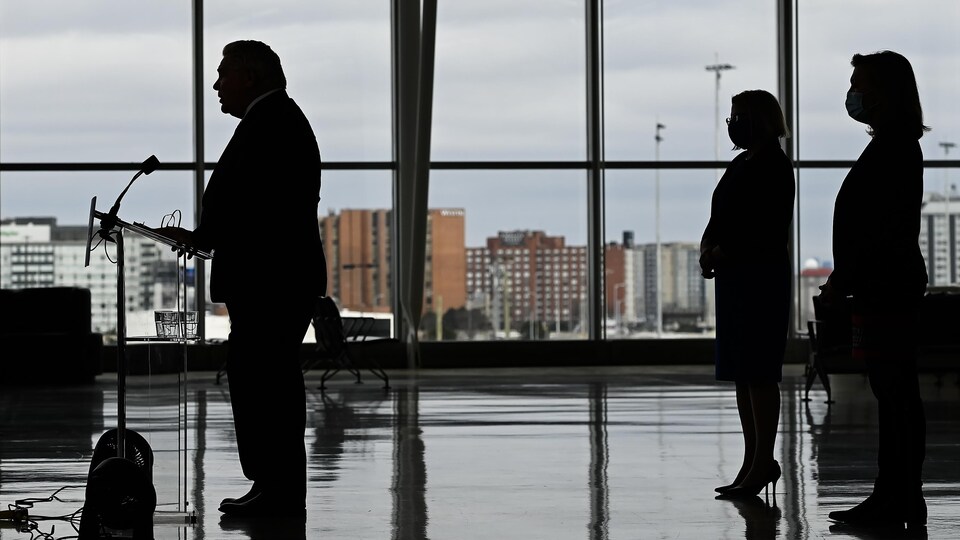 Doug Ford en contre-jour avec deux silhouettes féminines dans son dos.