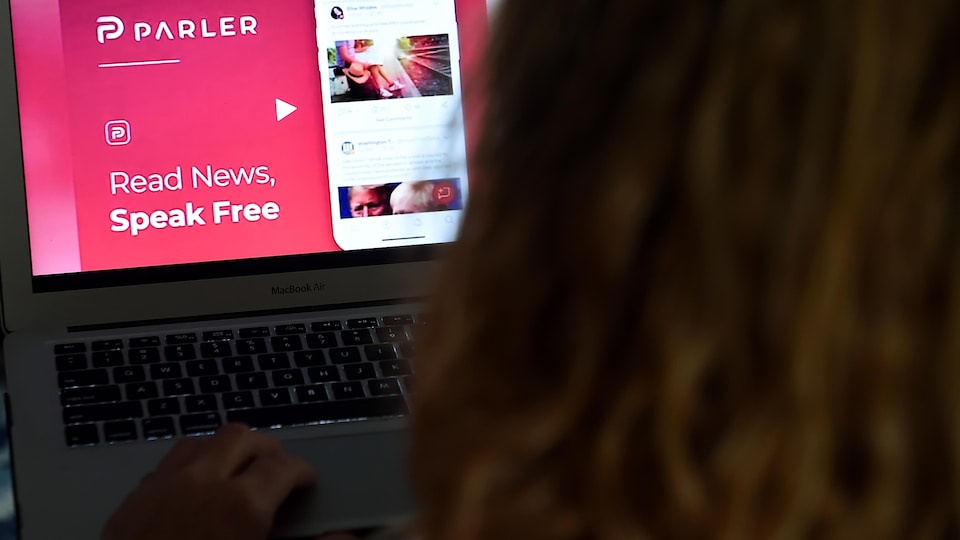 Une personne aux cheveux longs regarde l'écran d'un ordinateur portable, sur lequel est affichée la page d'accueil du réseau social Parler.