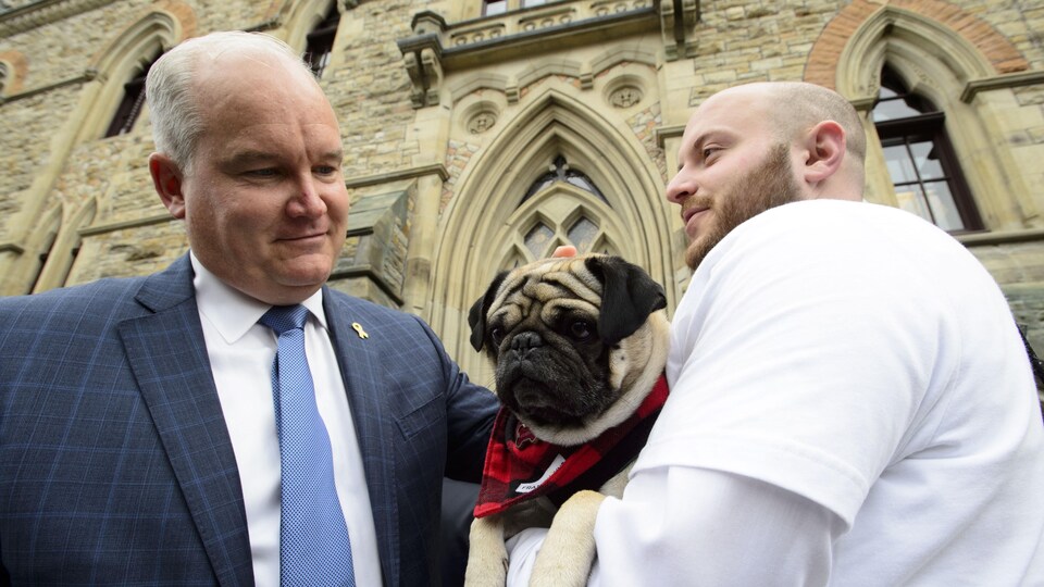 Erin O'Toole, un chien et un homme sont debout devant le parlement.