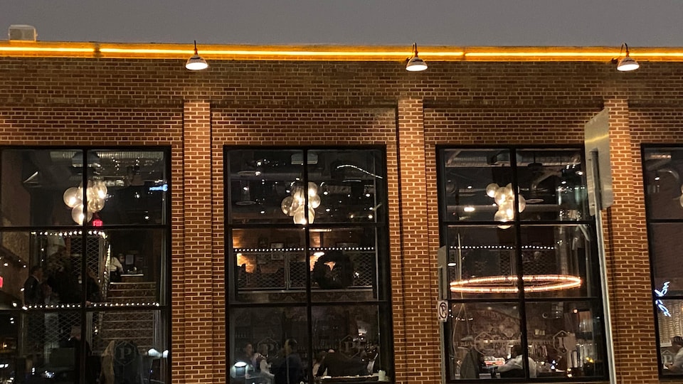 Extérieur du restaurant Parlour Italian Kitchen & Bar avec des fenêtres à travers lesquelles on voit plusieurs personnes sans masque. 