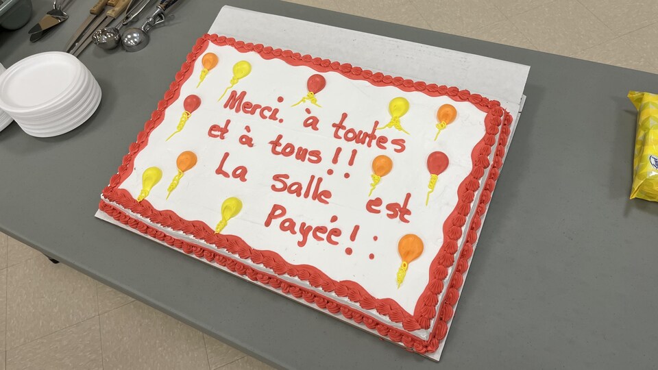 Un gâteau sur lequel il est écrit : Merci à toutes et à tous!! La salel est payée!