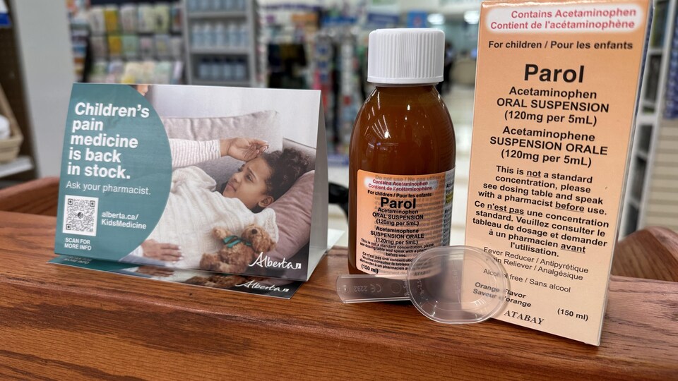 Une bouteille de médicament est posée sur une tablette à côté de sa boîte avec instruction et une cuillère graduée.
