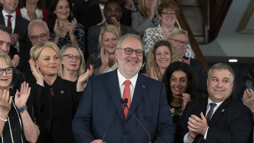Pierre Arcand, tout sourire, entouré par des membres du Parti libéral du Quebec qui l'applaudissent à la fin d'une conférence de presse. 
