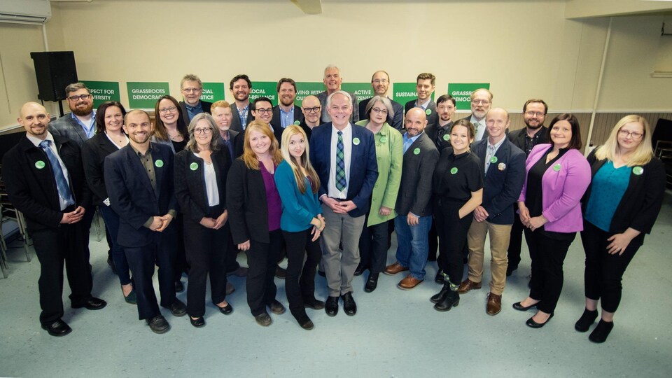 Des membres d'un parti politique se tiennent debout fièrement avec une épingle verte partisane sur leurs vestons.