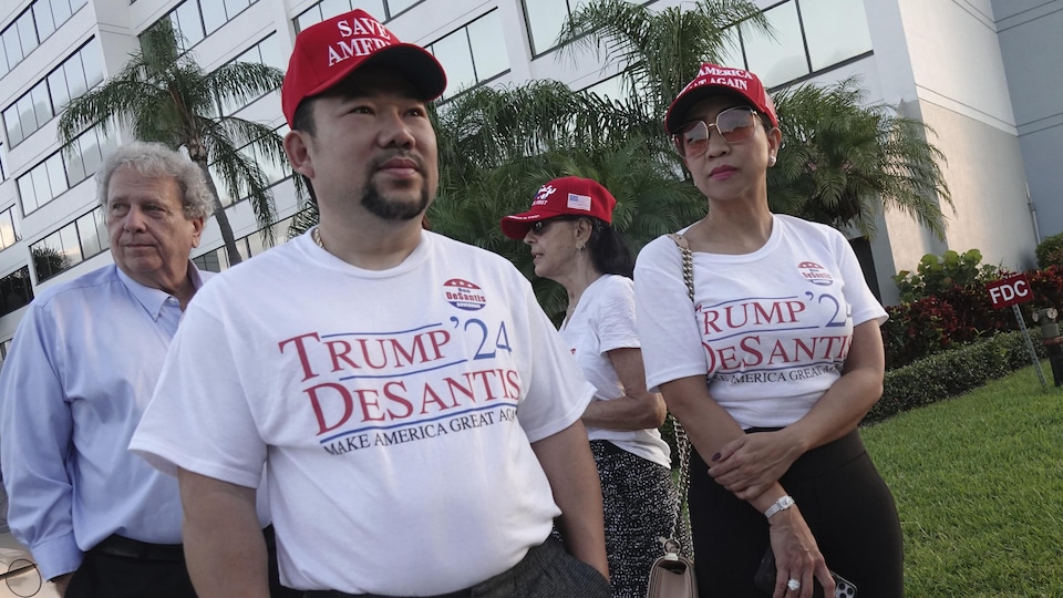 À l'avant-plan, deux partisans républicains portant des t-shirts qui portent deux inscriptions, « Trump-DeSantis en 2024 » et « Rendons à l'Amérique sa grandeur ».