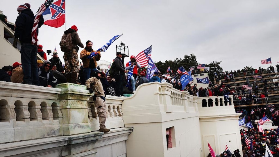Des partisans pro-Trump sont réunis, dont certains se trouvent debout ou accrochés à une palissade.