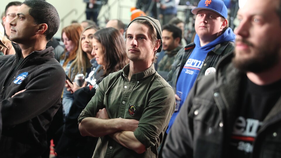 Des partisans de Bernie Sanders, debout, sont rassemblés dans un caucus de Des Moines, en Iowa. À l'avant-plan, on voit notamment un jeune avec une casquette à l'envers.