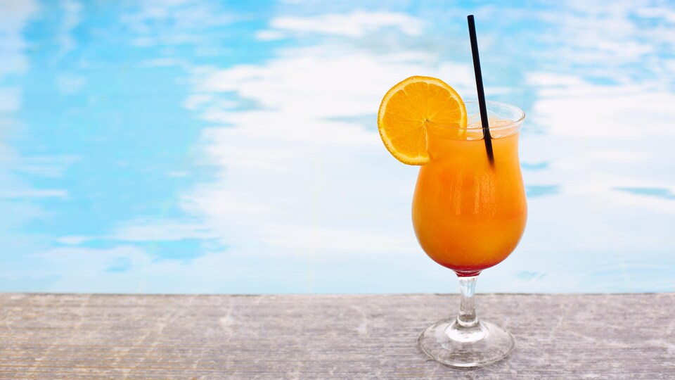 Un cocktail de couleur orange est déposé en bordure d'une piscine