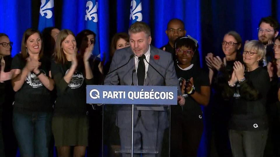 Pascal Bérubé est sur la scène et parle au micro, entouré de militants qui applaudissent.