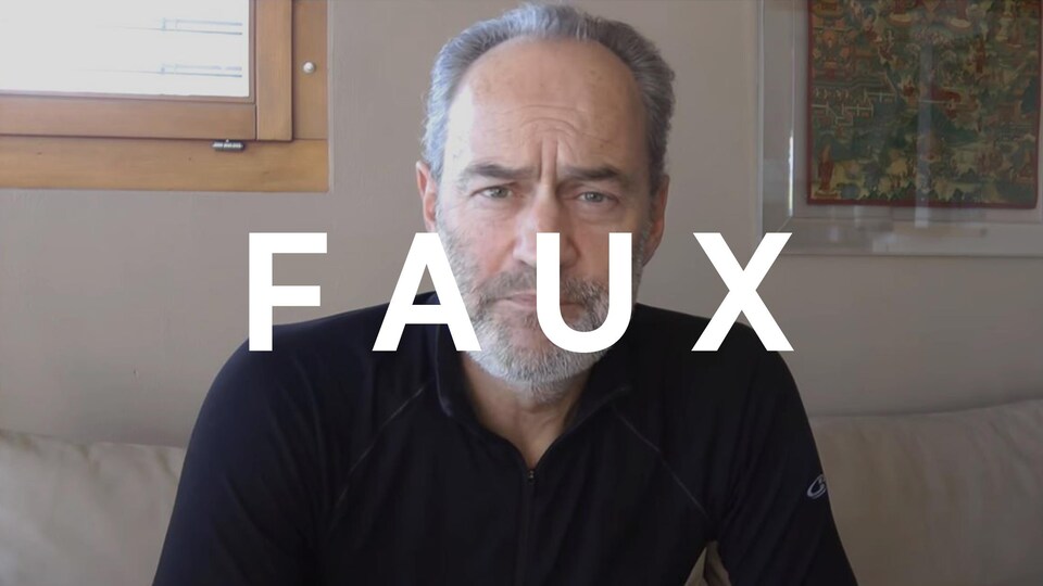 Un homme assis sur son divan qui parle devant la caméra.