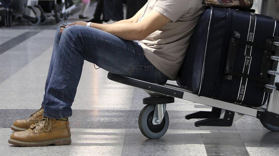Un homme assis dans un chariot à bagages attend à l'aéroport.