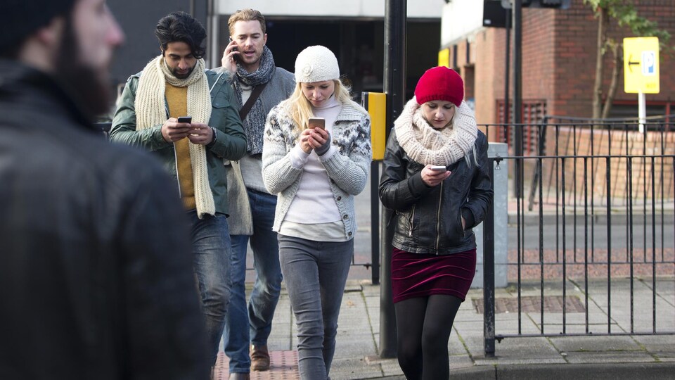 Trois d'entre eux regardent leur cellulaire tout en marchant, tandis qu'un autre parle au téléphone.
