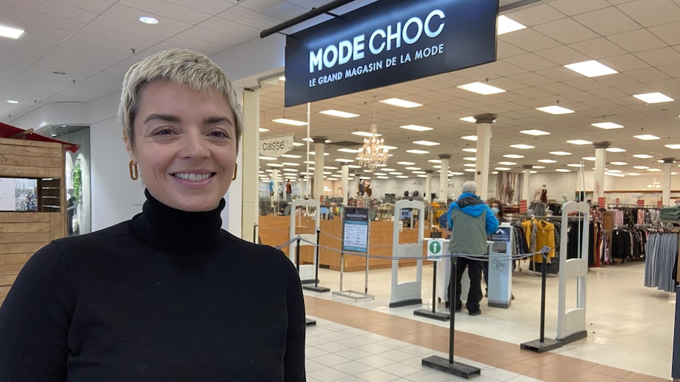 Une femme sourit devant un commerce, à l'intérieur d'un centre commercial.