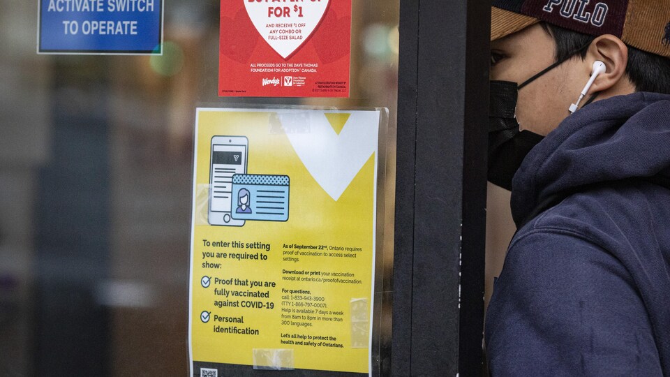 Un client entre à l'intérieur d'un restaurant; une affiche sur la porte dit qu'il doit montrer une preuve de vaccination.