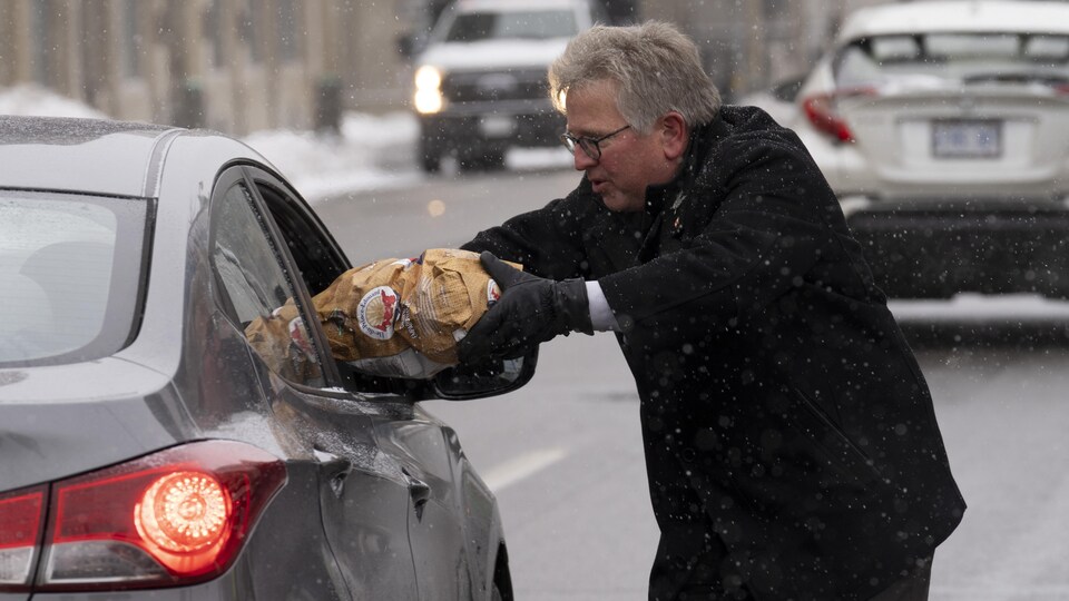 Un homme dans la rue passe un sac de patates par la fenêtre d'une voiture pour le donner à ses occupants.