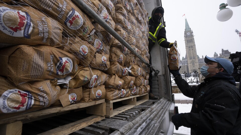 Devant le Parlement d'Ottawa, un homme dans un semi-remorque plein de patates tend un sac de pommes de terre à une autre personne debout derrière le camion.