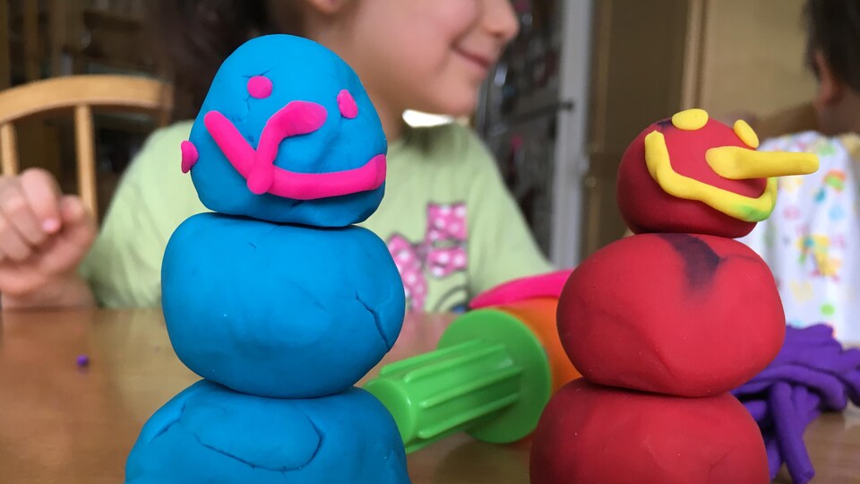 Deux bonhommes de neige en pâte à modeler avec des enfants en arrière plan.