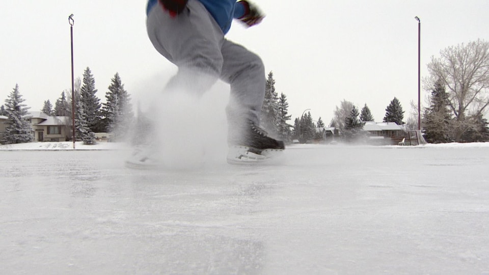 Un homme fait voler la glace en freinant sur une patinoire extérieure. 